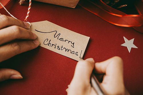 Female hands writing Merry Christmas on tag for the gift