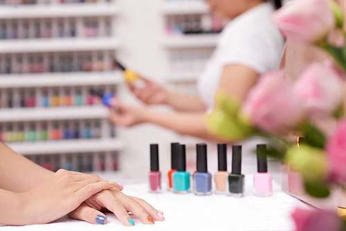 Hands of female client with colorful nails in manicure salon