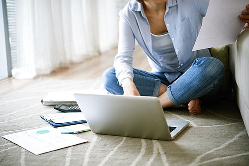 Cropped image of woman sitting on the floor in her house and working with documents