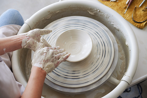 Hands of potter making a plate out of white clay