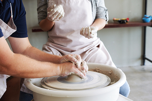 Master teaching apprentice how to work on pottery wheel