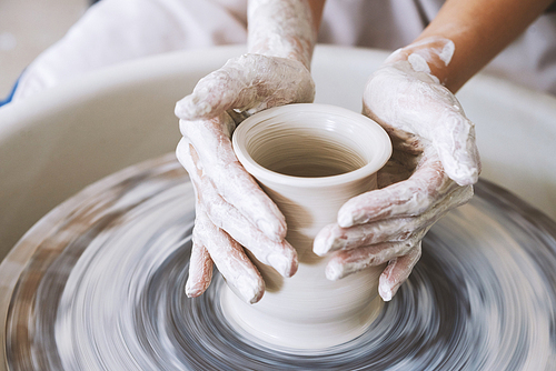 Close-up image of craftwoman making white clay pot