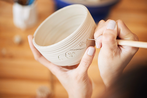 Potter using stylus to make ornament on clay cup