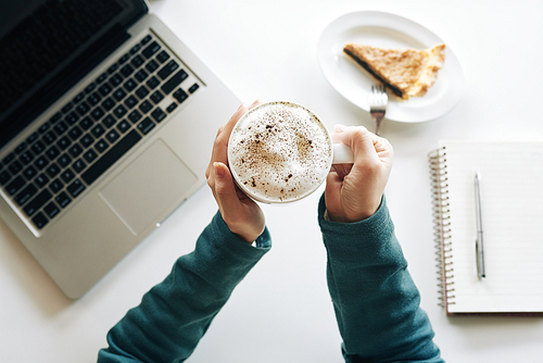 Cup of cappuccino with foam in hands of young woman