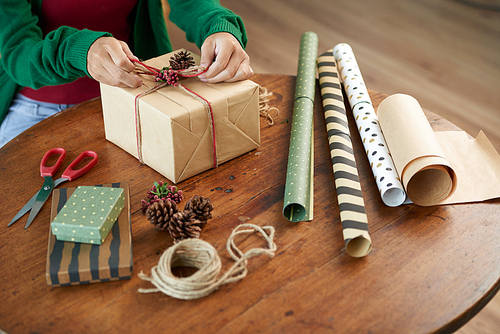 Creative woman using craft paper, berries and cones when wrapping present