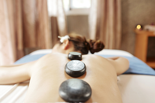 Young woman relaxing in spa salon with hot stones on her bask