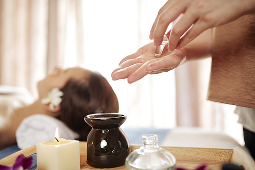 Masseur putting oil in hands to warm it up before applyingon face of female client