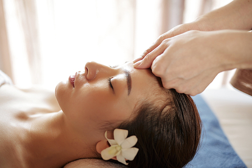 Beautician massaging forehead of young beautiful Vietnamese woman