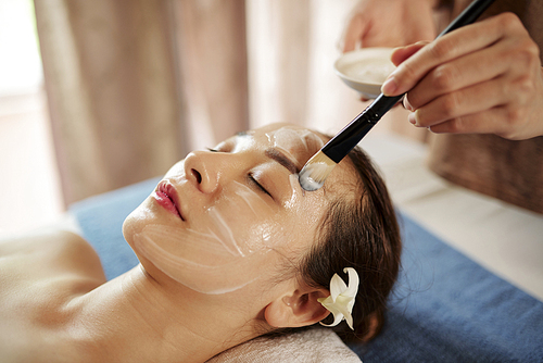 Close-up image of young Vietnamese woman getting anti-aging face treatment in spa salon