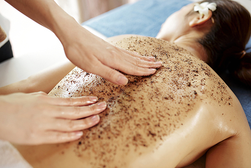 Hands of beautician applying apricot kernel scrub on back young beautiful woman in spa salon