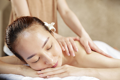 Young Vietnamese woman enjoying relaxing back massage in spa salon