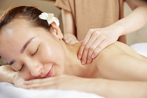 Smiling young beautiful Asian woman enjoying healing neck and shoulders massage