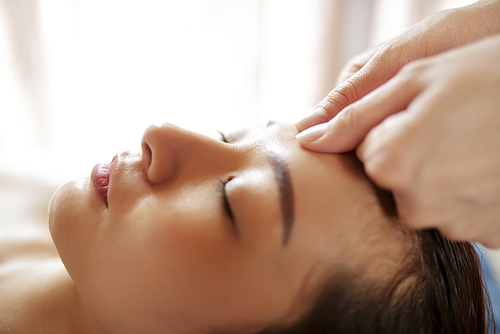 Close-up image of calm young Asian getting relaxing face massage with oils