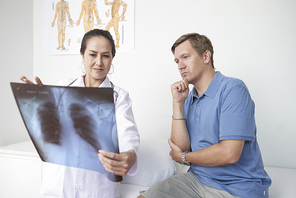 Female Vietnamese doctor showing lungs x-ray to mature patient