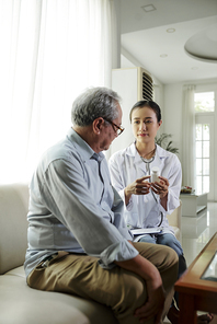 Asian young doctor sitting on sofa with senior man suggesting good pills from disease and talking about his treatment while visiting him at home