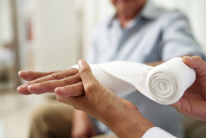 Close-up of nurse holding and bandaging hand of senior patient at hospital