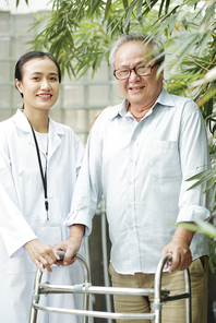 Portrait of senior man with walker and Asian female doctor in white coat standing outdoors and smiling at camera