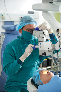 Female patient lying under surgical microscope while surgeon doing vision correction in operating room