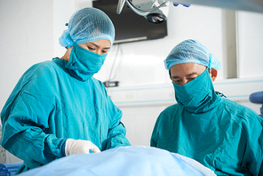 Professional surgeon and his assistant wearing uniform standing at operation in operating room at hospital