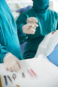 Close-up of surgeons in uniform and protective gloves using medical tools to operate the patient on the table in operating room