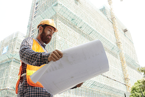 Professional civil engineer in hard hat examining blueprint of building