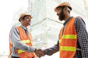 Smiling construction workers shaking hands to greet each other before day of working day