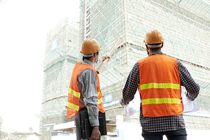 Contractor pointing at building at explaining something to construction worker