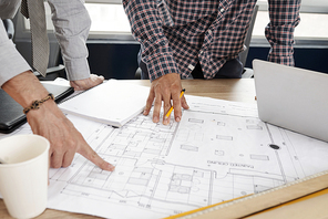 Team of construction engineers discussing paper blueprint on office table