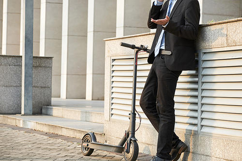 Close-up of businessman standing in suit talking on mobile phone and gesturing while riding on scooter in the city