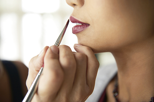 Close-up of cosmetician applying lipstick with brush on lips of fashion model