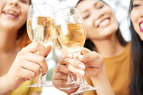 Close-up of glasses with champagne holding by happy young women, they toasting and celebrating the holiday