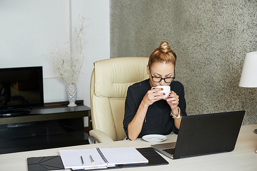 Business lady enjoyng cup of coffee ahwer reading e-mails on laptop screen