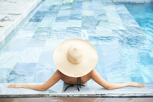 Young woman in straw hat resting in swimming pool, view from above