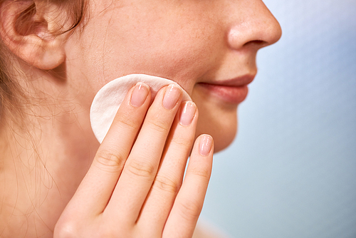 Close-up of young woman with perfect face skin cleaning her face with cotton pad