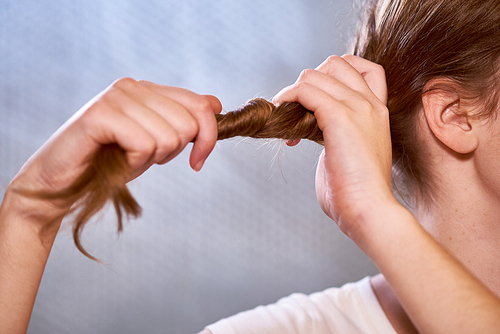 Close-up of young woman holding her long clean healthy hair with hands to make a hairstyle