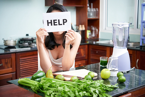 Young woman standing near the kitchen table with vegetables holding placard with help text and is going to prepare a salad