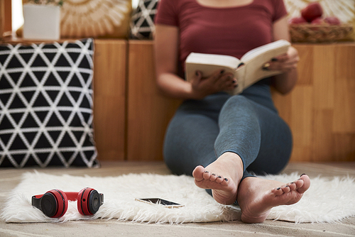 Barefoot young woman sitting of floor at home and reading good book