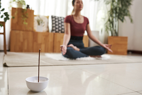 Small ball with burning aroma stick on floor of young meditating woman