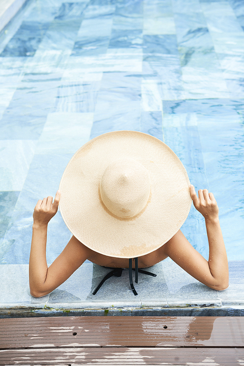Woman in big straw hat relaxing in swiming pool with tourquoise water , view from above