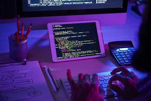 Software developer working with decoded information in tablet while sitting in front of computer monitor