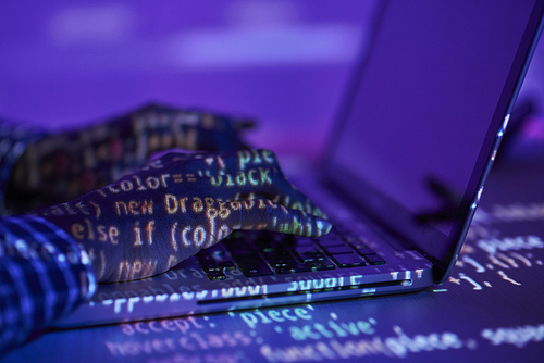 Reflection of electronic data on hands of programmer typing on laptop keypad by desk