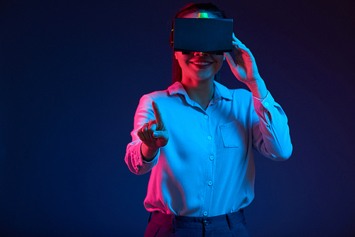 Smiling young Vietnamese businesswoman in virtual reality glasses pushing button of invisible interface