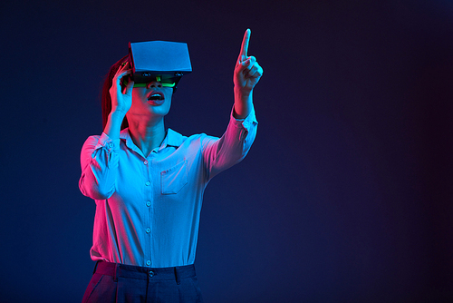 Young curious businesswoman pointing at button of modern interface when working in virtual reality glasses