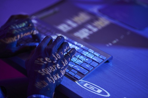 Close-up of programmer typing on computer keyboard and working with new software while sitting at the table in dark office