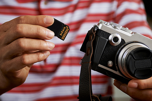 Close-up of mature photographer holding digital camera and inserting the SD memory card into the camera