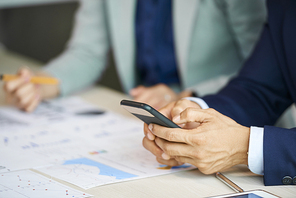 Hands of businessman texting friends or colleagues when sitting at meeting table