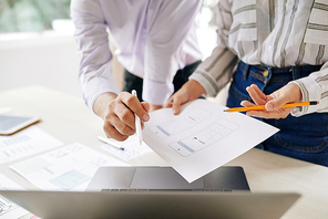 Two young contemporary managers discussing paper with gadget scheme or instruction of smartphone and consulting online data