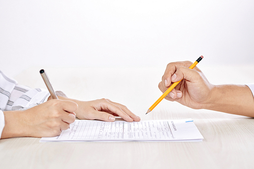 Hand of agent with pencil pointing at contract or other paper while client signing it after making deal
