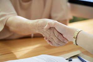 Close-up image of social worker shaking hand of aged woman