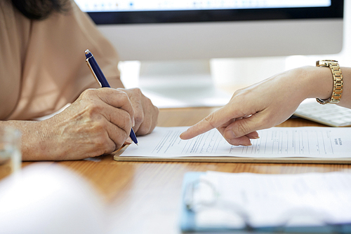 Hand of insurance agent showing senior woman where to sign the contract